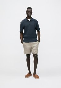 Mørkeblå ribbestrikket poloskjorte med korte ermer, kombinert med beige shorts og brune slip-on sko. Rent design med en avslappet passform.