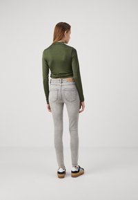 Zöld, hosszú ujjú felső, összegyűrt hátrészsel, világosszürke skinny farmernadrággal és fekete sportcipővel, fehér csíkokkal és világosbarna talppal párosítva.