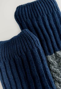 Mangas de pierna de punto azul marino con textura acanalada y un detalle de punto en cable en un gris más claro. Material suave y acogedor.