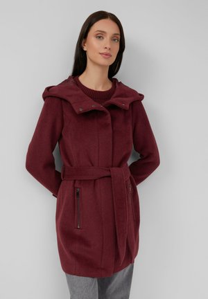 Bordeaux lange jas met een grote capuchon, een riem in de taille, ritszakken aan de zijkanten en een zachte textuur. Heeft een geribbelde kraag eronder.