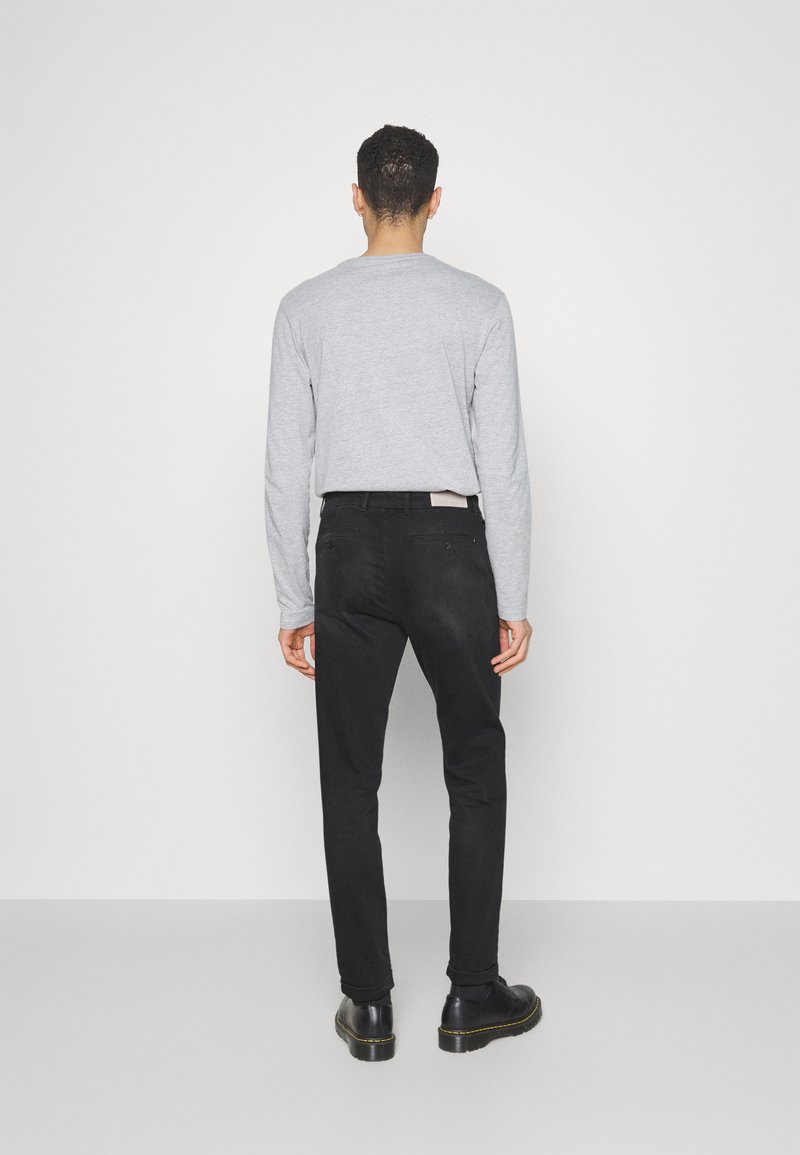 GrauesLangarmshirt, schwarze Slim-Fit-Hose, Lederschuhe. Schlichtes Design, keine Muster. Rückansicht, minimalistischer Hintergrund.