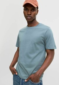 Light blue cotton t-shirt with short sleeves and a round neckline, paired with denim jeans. A faded peach cap completes the look.