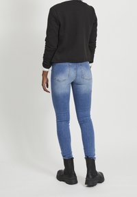 Černý prošívaný zkrácený svetr, modré vybledlé skinny džíny a černé kotníkové boty, pohled zezadu.