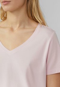 Jasnoróżowa koszulka typu V-neck wykonana z miękkiej bawełny. Krótkie rękawy i gładka tekstura; minimalne wykończenie przy dekolcie.