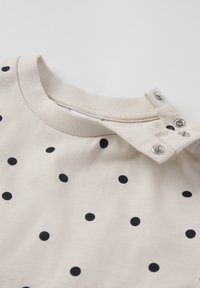 Beige katoenen shirt met gelijkmatig verspreide marineblauwe polka dots, met een ronde hals en drukknopen op de schouder voor gemakkelijk aan- en uittrekken.