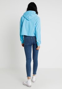 Felpa corta azzurro chiaro con cappuccio, abbinata a jeans attillati blu e scarpe da ginnastica alte bianche. Tessuto morbido, design casual.