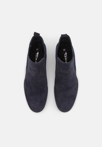 Un paio di ankle boots slip-on in camoscio blu navy con pannelli laterali elasticizzati, esposti dall'alto su uno sfondo bianco semplice.