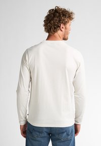 Camisa de manga larga en beige claro, con un cuello redondo simple y textura suave, combinada con jeans de denim azul.