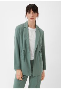Muntgroene blazer met trekkoordaccenten, lichte stof, op maat gemaakte snit, reverskraag en voorzakken, gecombineerd met een witte top.