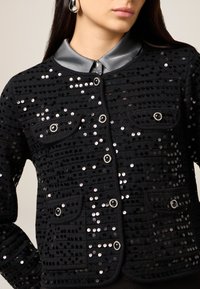 Schwarze, mit Pailletten verzierte Jacke mit Satin-Kragen, zwei aufgesetzten Taschen, silberfarbenen Knöpfen und strukturiertem Stoffdesign.