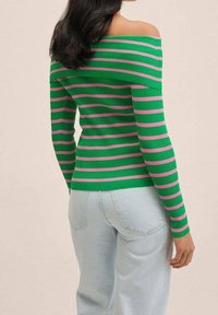 Pull côtelé rayé vert et rose avec un design épaules dénudées, une coupe ajustée et des manches longues, associé à un jean bleu clair.