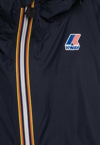 Tmavě modrá bunda K-Way s celopropínacím zipem v červené, žluté a tmavě modré barvě, s logem v modré, červené a bílé. Lehký, hladký materiál.