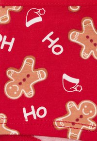Czerwona tkanina z wzorem piernikowych ludzików, śnieżnych czapek i napisem „HO” w białym kolorze. Wzór ma zabawny, świąteczny motyw.