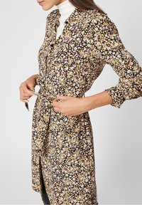 Abito a stampa floreale con sfondo nero e fiori rosa e gialli sparsi, chiusura con bottoni frontale, vita cinchata e maniche lunghe.