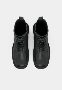 Μαύρες δερμάτινες μπότες έως τον αστράγαλο με λεία υφή, που διαθέτουν κλείσιμο με κορδόνια, επίπεδες σόλες και βρόχο στον λαιμό για εύκολη χρήση.