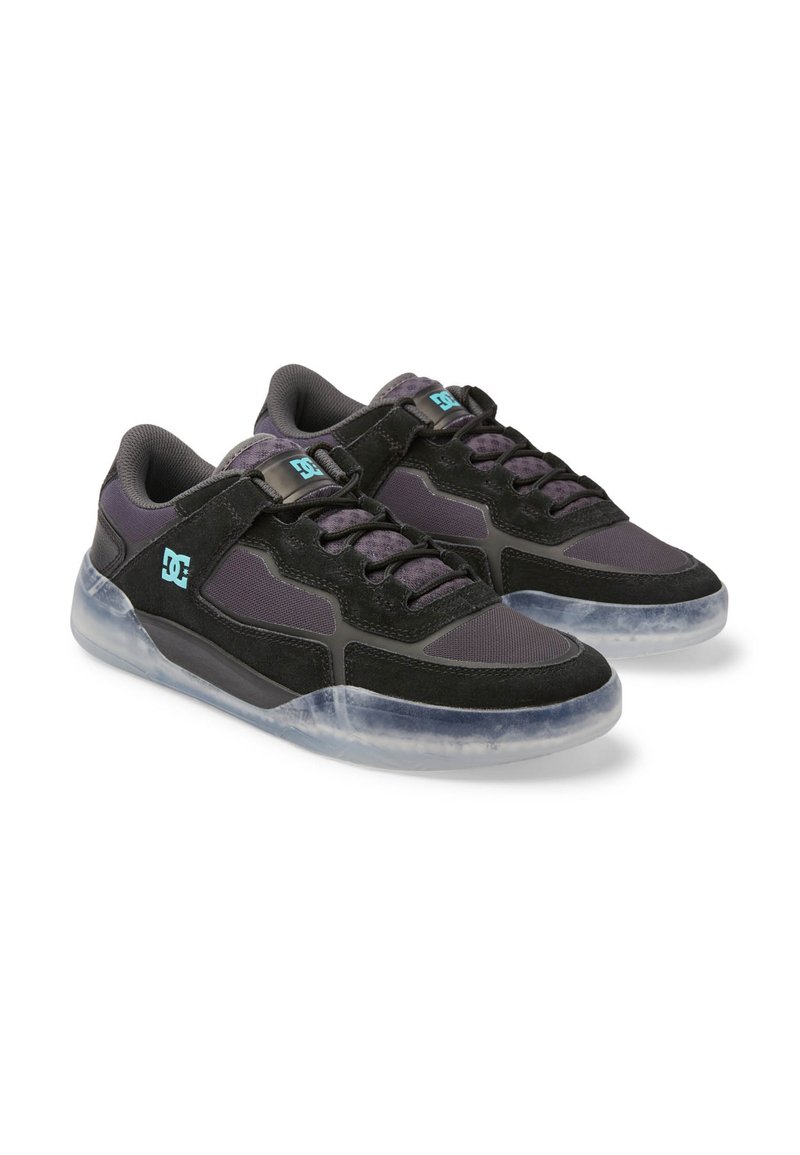 Sneakers low-top neri e viola scuro con logo DC blu chiaro, lacci e suole trasparenti, mostrati in un paio su sfondo bianco.