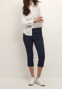 Wit overhemd met knopen gecombineerd met marineblauwe cropped broek. De outfit is gemaakt van glad, lichtgewicht materiaal en wordt aangevuld met witte sneakers.