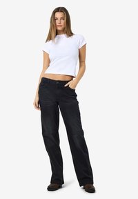 Zwarte denim jeans met een rechte pijp, gecombineerd met een witte, aansluitende t-shirt met korte mouwen. Model draagt bruine enkellaarsjes.