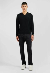 Pull noir à col en V en maille lisse, associé à un jean sombre ajusté et des baskets blanches. Design simple, avec peu de détails.