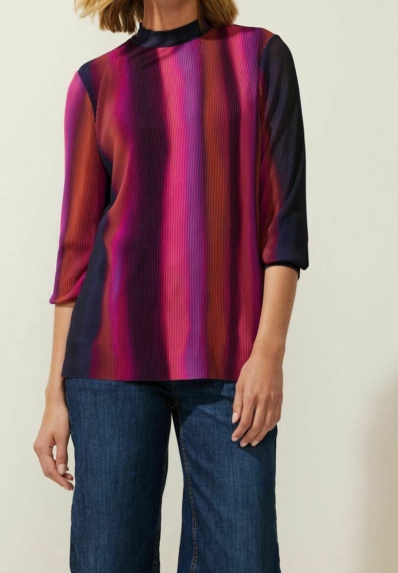 Multikleurige geribde blouse met een hoge hals, met roze, paars en blauwe verticale strepen; driekwartmouwen; gecombineerd met denim.