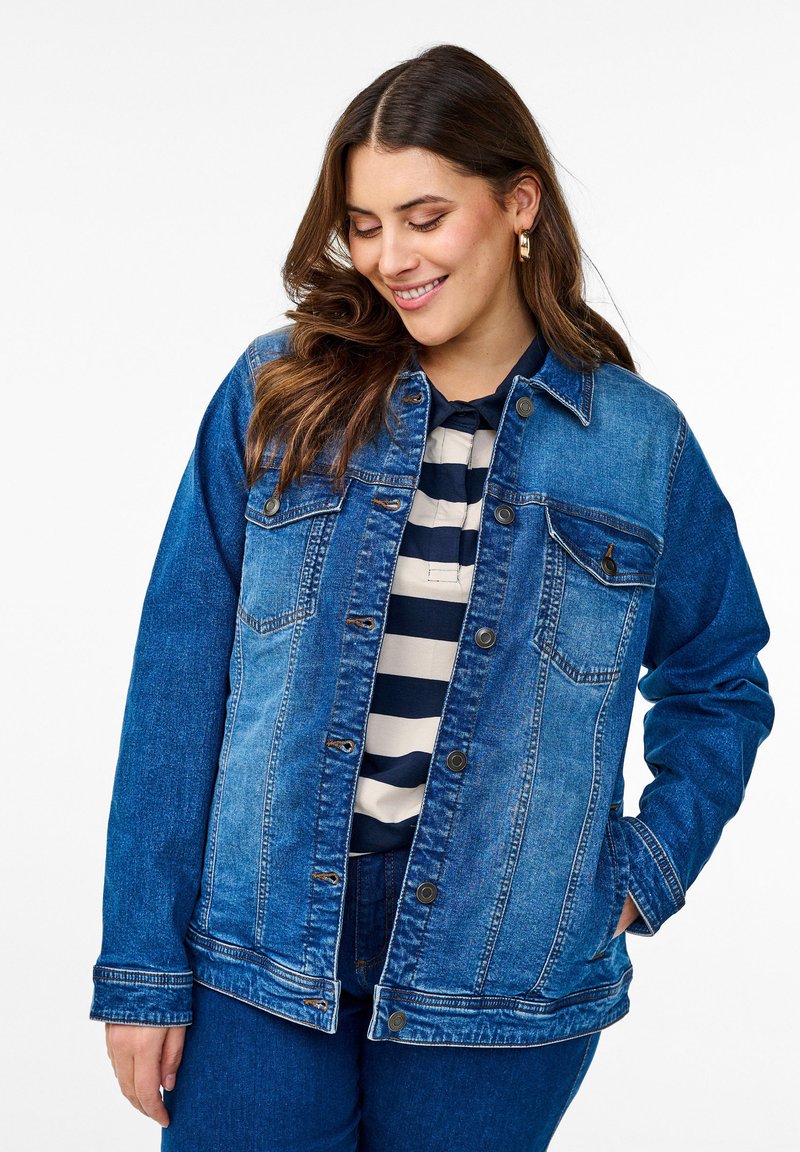 Traper jakna u raznim nijansama plave boje s klasičnim krojem, dugmadi sprijeda, dva džepa na prsima i dugim rukavima. Nošena preko majice s prugama.