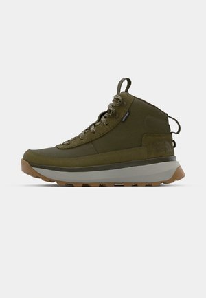 Trekking boots in olive green featuring a textured suede upper, grey midsole, rugged outsole, and reflective laces for enhanced visibility.