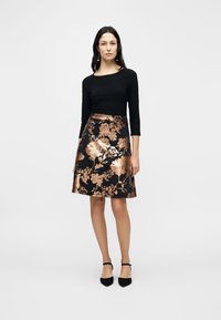 Μαύρο τοπ με μακριά μανίκια σε συνδυασμό με φούστα έως το γόνατο με χρυσαφένιο λουλουδένιο σχέδιο. Η φούστα έχει ομαλή υφή και στενή μέση.