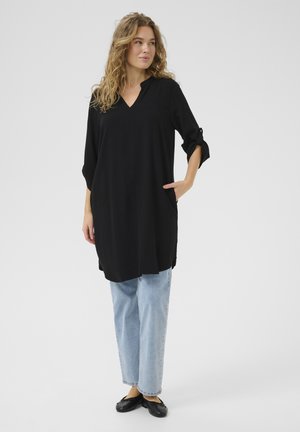 Tunique noire avec un col en V et des manches trois quarts, dotée de poches latérales et d'une coupe décontractée, associée à un jean bleu clair et des ballerines noires.