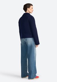 Giacca cropped navy in misto lana con colletto a punta; abbinata a jeans in denim azzurro a gamba larga e scarpe rosse.