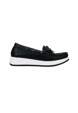 Zapato negro de cuero tipo slip-on con punta redondeada, suela de goma blanca, acento de lazo y ojales decorativos de metal a lo largo del costado.