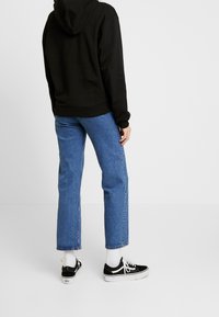 Sudadera negra con bolsillo canguro, jeans rectos azules y zapatillas negras y blancas con cordones blancos y suelas texturizadas.