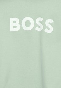 Světlově zelená bavlněná mikina s výrazným bílým nápisem "BOSS" přes přední část. Měkká textura, minimalistický design.