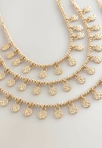 Guld-färgad lagerhalsband med pärlkedjor och små, texturerade cirkulära hängen som hänger med intervall längs trådarna.