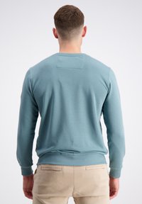 Ljusblå sweatshirt med rund halsringning, långa  ärmar, ribbade muddar och nederkant, slät textur, ryggsömmens detaljer vid axlarna. Bärs med beige byxor.