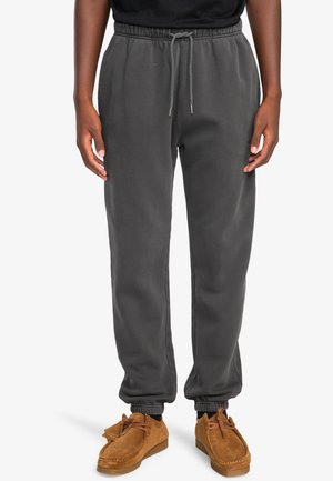 Dark gray sweatpants with elastic waistband and adjustable drawstring. Cuffed ankles and soft texture. Worn with brown moccasin-style shoes.