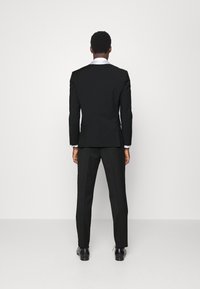 Zwart op maat gemaakt pak met een enkele split, slim-fit broeken en contrasterende witte kraag. Gladde stoftextuur, gepolijste zwarte schoenen.