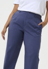 Pantalons tailleurs bleu avec fermeture à bouton, poches latérales, texture lisse et coupe droite.
