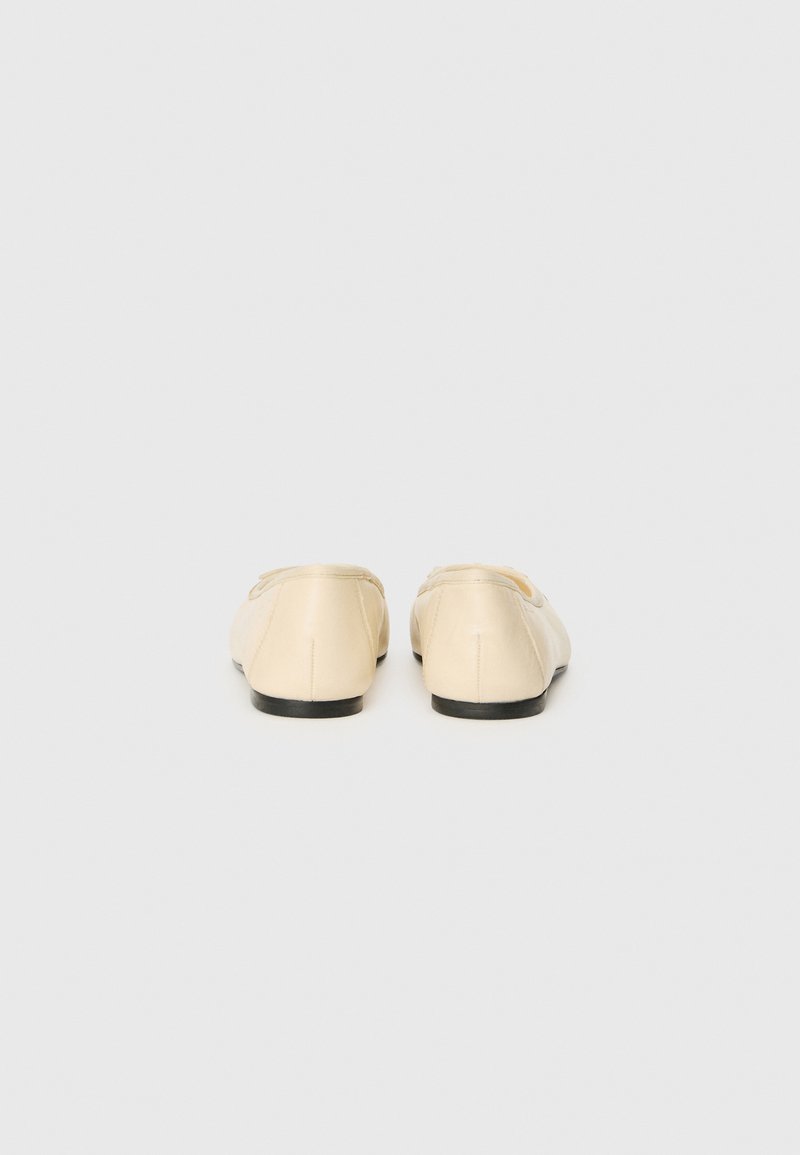 Ballerines beige avec une finition satinée lisse, un bout arrondi et un design minimaliste. Semelle en caoutchouc noir visible de l'arrière.