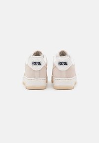 Beige Nike sneakers with suede material, white fluffy collar, featuring black logo on heel, and textured rubber sole.