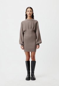 Abito in maglia a coste color taupe con vita aderente e maniche a palloncino, abbinato a stivali neri al ginocchio con suole spesse.