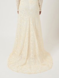 Μακριά ελεφαντόδοντη δαντελένια φόρεμα με περίπλοκα λουλουδάτα κεντήματα και μια ρέουσα ουρά. Μακριά μανίκια με λουλουδάτα σχέδια ενισχύουν τον κομψό σχεδιασμό.