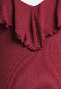 Top burguinhô com textura canelada, decote com babados e corte ajustado. Não apresenta outros padrões ou detalhes em metal.