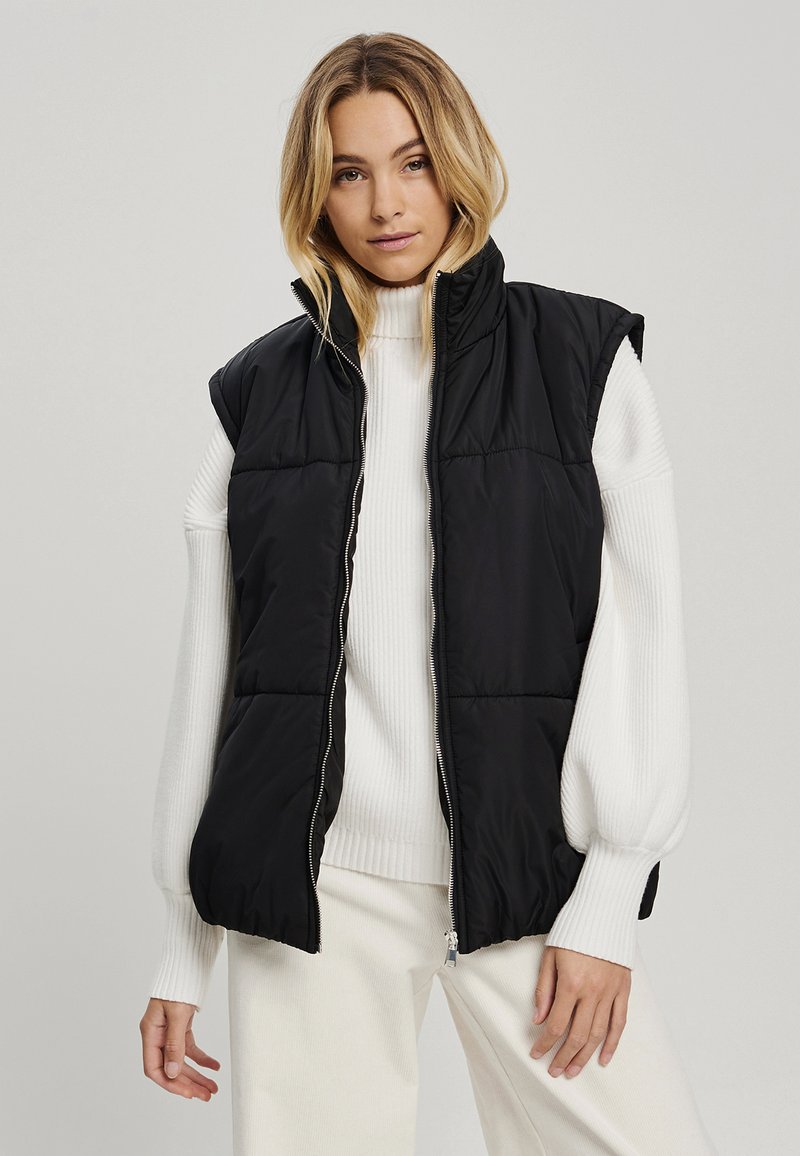 Must must vest kõrgema kraega, käiseid pole, ees lukk. Kanda valge ribakudumi üle. Sile tekstuur.