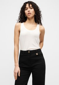 Λευκό αμάνικο τοπ με στρογγυλεμένο ντεκολτέ, συνδυασμένο με μαύρο παντελόνι που έχει λεπτομέρειες με χρυσούς κουμπιά και λογότυπο.