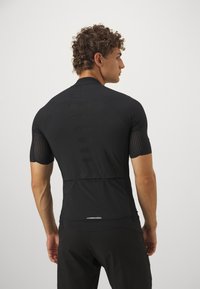 Svart treningstrøye med kort erm, med en teksturert strikket design, mesh-seksjoner på ermene og en baklomme for oppbevaring.