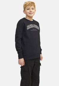 Czarny sweatshirt z długimi rękawami, z białym logotypem "JACK & JONES". Noszony z czarnymi spodniami cargo, teksturowany materiał, dopasowane mankiety.