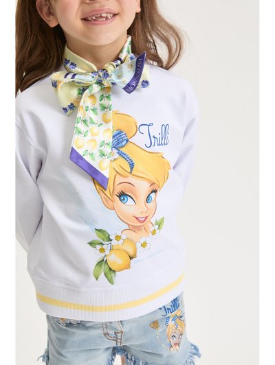 Χαμογελαστό παιδί που φοράει λευκό φούτερ και τζιν σορτς με σχεδιασμούς Τίνκερ Μπελ και λεμονιών, και φουλάρι με λουλουδάτο μοτίβο δεμένο γύρω από τον λαιμό.