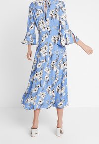 Blue floral dress featuring bell sleeves, a keyhole back, and a flowing silhouette with white and brown floral patterns on a soft fabric.