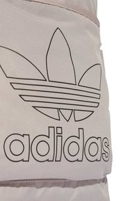 Primer plano de tela beige con el logo en trébol negro de Adidas y el nombre de la marca impresos en un material texturizado.