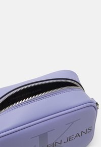 Fialová kabelka z umělé kůže s hladkou texturou, zipovým uzávěrem a stříbrným kováním s černým logem "CALVIN KLEIN JEANS".